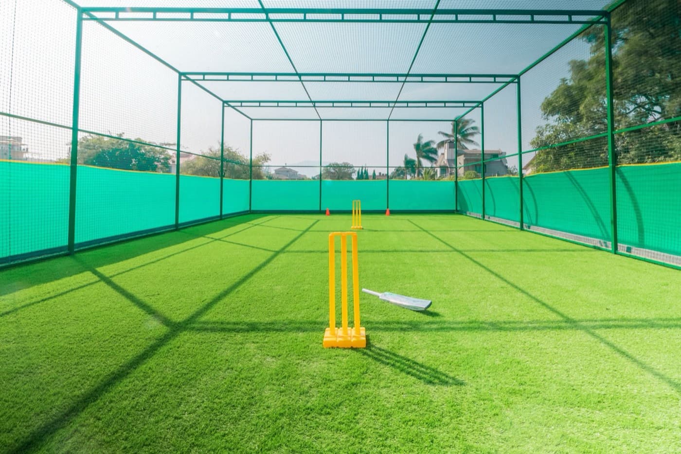 An empty netted practice lane with stumps and a bat